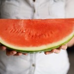 A person holding a big wedge of seedless watermelon