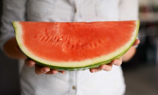 A person holding a big wedge of seedless watermelon