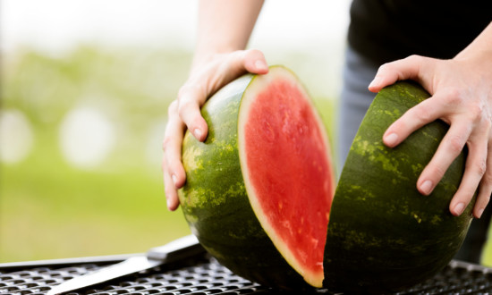 watermelon on table cut in half with person holding each side. knife on table