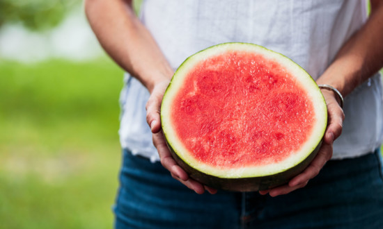 person holding watermelon half, bright red flesh