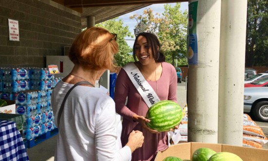watermelon queen smiling at customer at outside event in front of watermelon bin