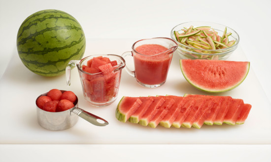various forms of watermelon set on white cutting board - mini, balls in measuring cut, chunks and puree in measuring cups, rind cuts in bowl, wedge and slices, triangular cut