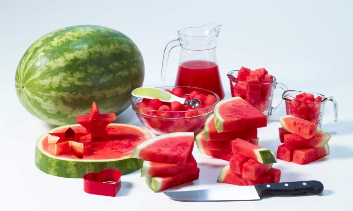 various forms of watermelon on white background - whole, slice star cutout with cutter, puree, balls with melon baller, diced and sticks. knife in foreground