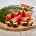 half watermelon cut into sticks on top of round wooden cutting board