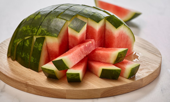 half watermelon cut into sticks on top of round wooden cutting board