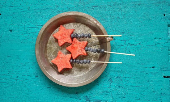 skewered watermelon cutouts (stars) skewered with blueberries set in metal tray on teal wooden background