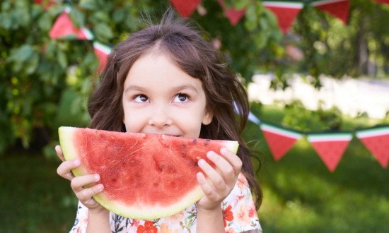 young girl holding watermelon slice with watermelon streamers in background, outdoors