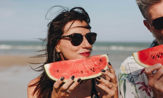 woman and man at beach holding watermelon wedges