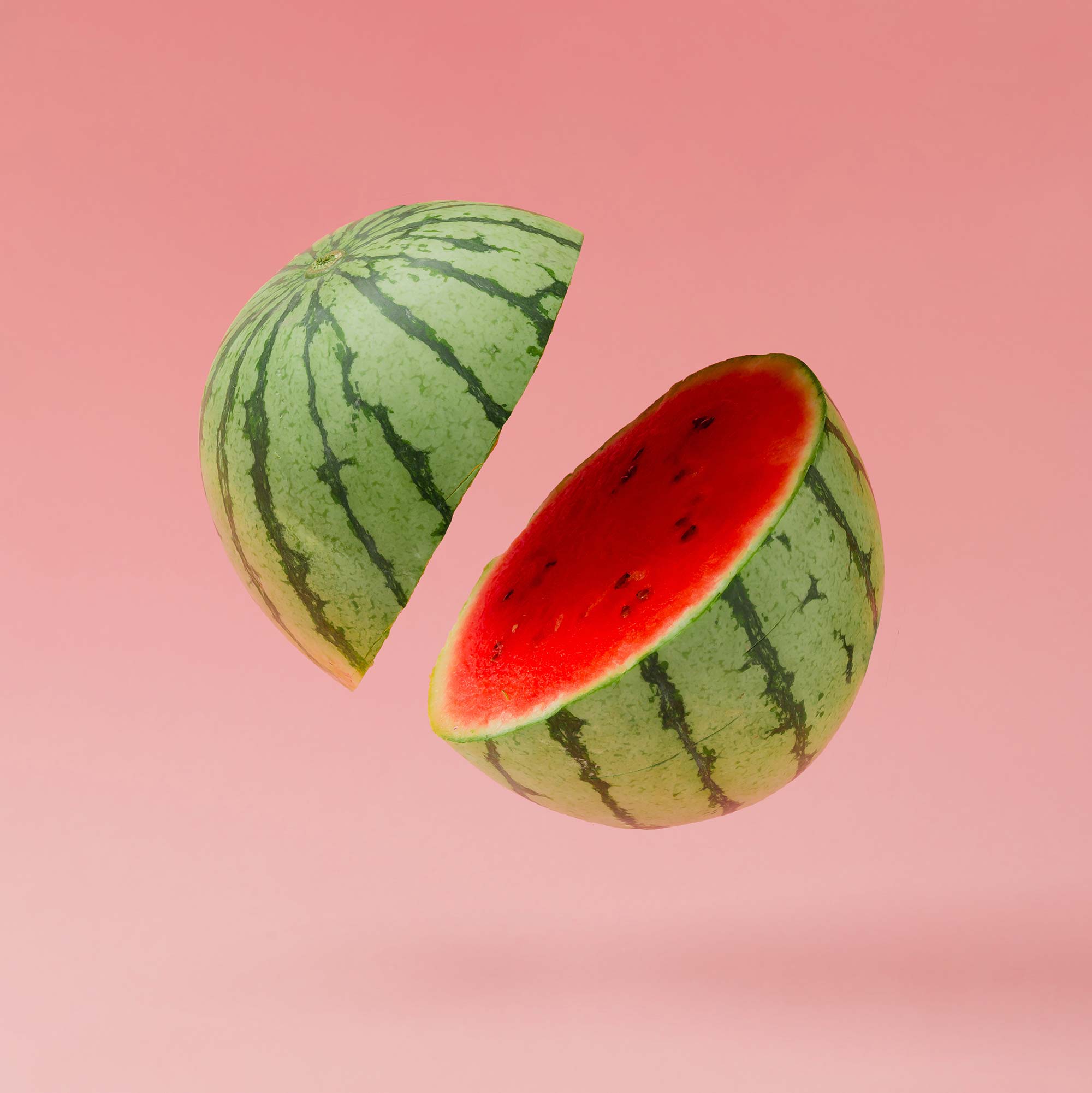 watermelon, cut in half, seemingly suspended in air with variegated pink background