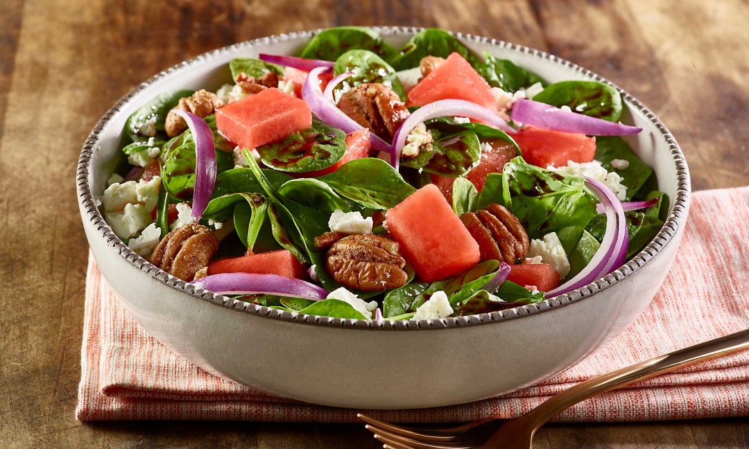 watermelon salad set in salad bowl on cloth napkin, fork on side on wooden cutting board