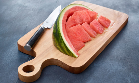 watermelon wedge with flesh cut away from rind on wooden cutting board with knife on side