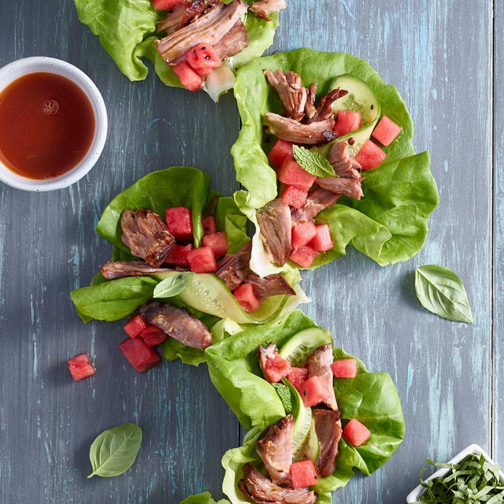 watermelon lettuce wraps with condiments and cruet of sauce set on blue-gray wooden background