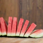 Accordion slices (triangular cuts) of red watermelon on wooden cutting board