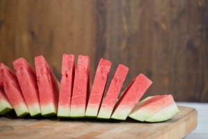 Accordion slices (triangular cuts) of red watermelon on wooden cutting board