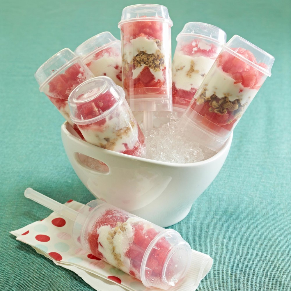 Breakfast Push Pops set in round bowl set with crushed ice holding 5 push pops. One push pop in foreground on white and red polka dot paper napkin. Set on teal green tablecloth