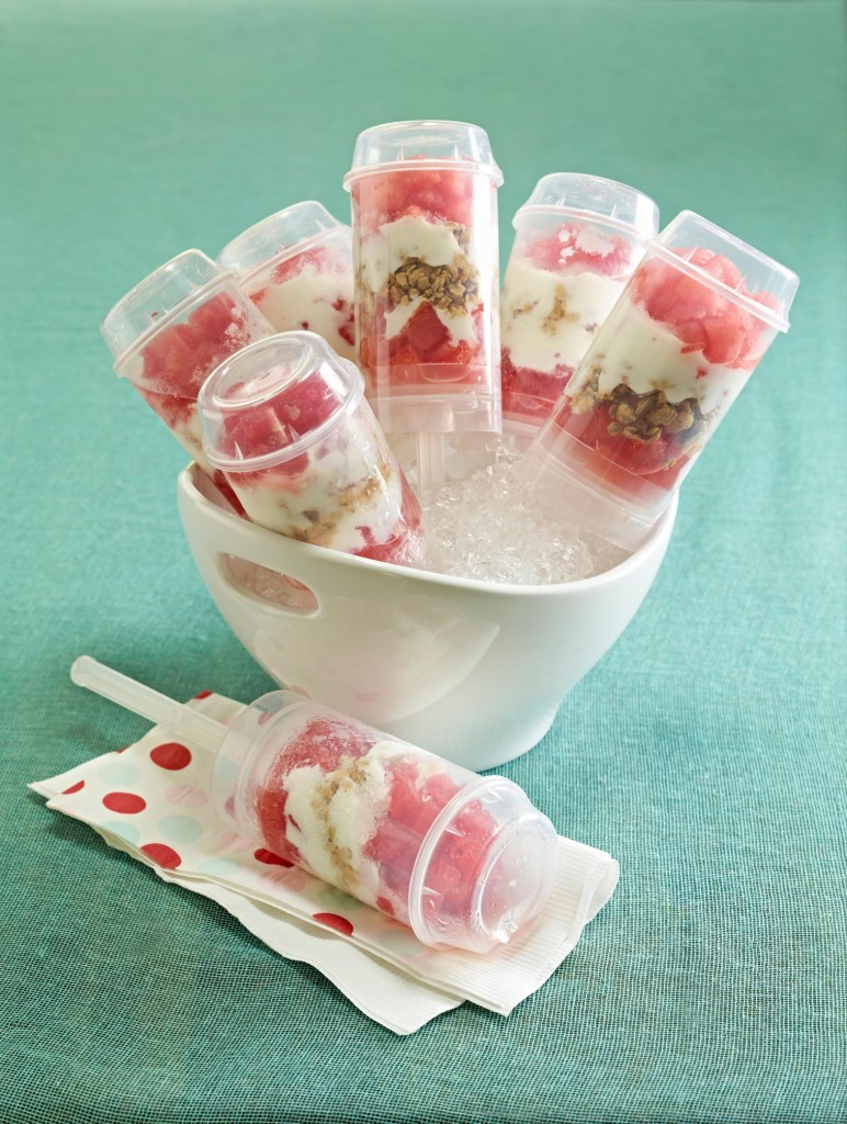 Breakfast Push Pops set in round bowl set with crushed ice holding 5 push pops. One push pop in foreground on white and red polka dot paper napkin. Set on teal green tablecloth