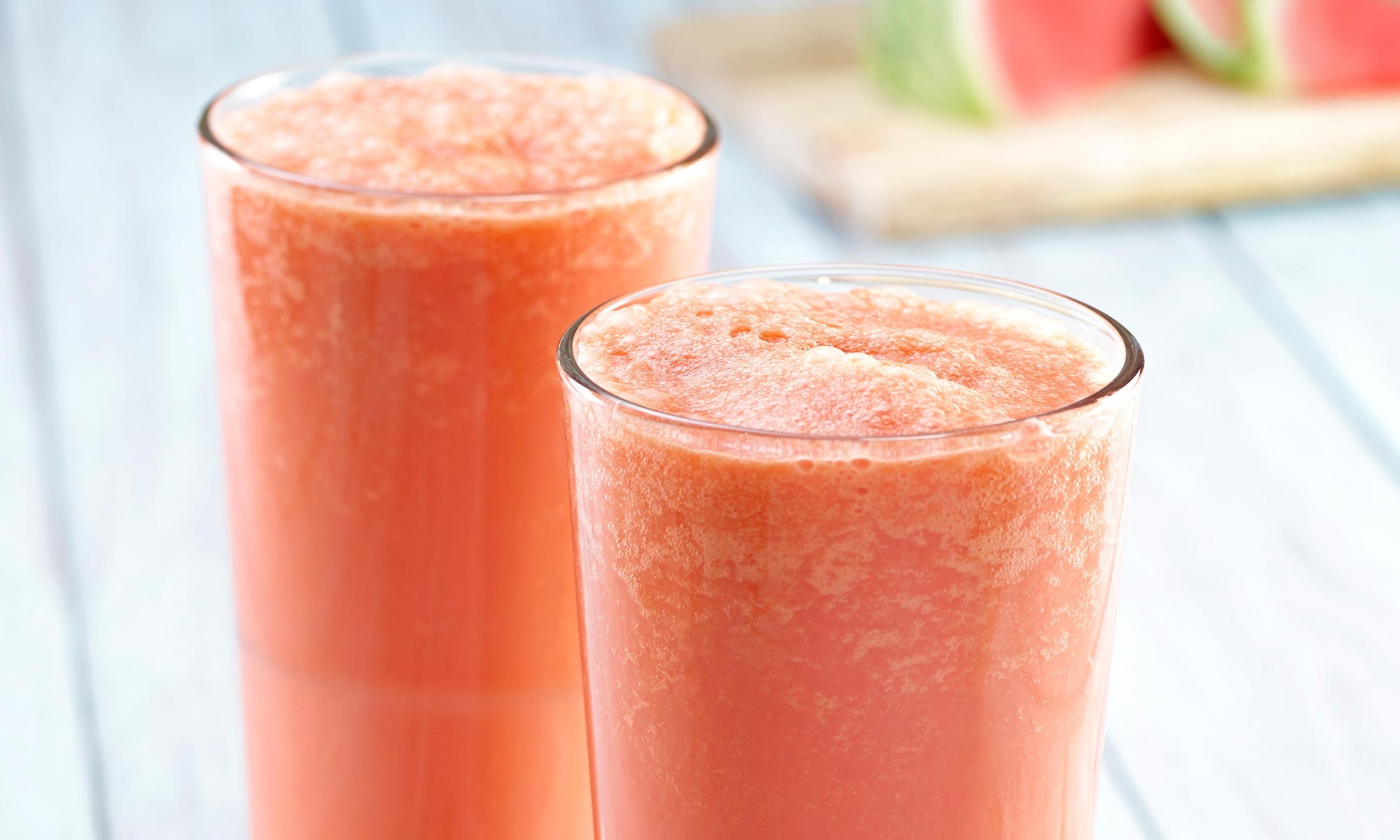 Collagen creamsicles (x2) in tall clear glasses with straws and greens garnish on side. Watermelon wedge and slices in background on wooden cutting board.