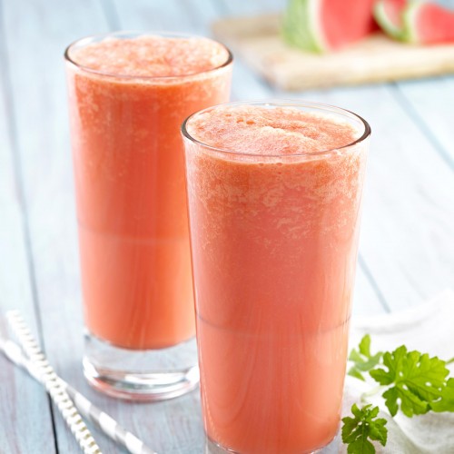 Collagen creamsicles (x2) in tall clear glasses with straws and greens garnish on side. Watermelon wedge and slices in background on wooden cutting board.