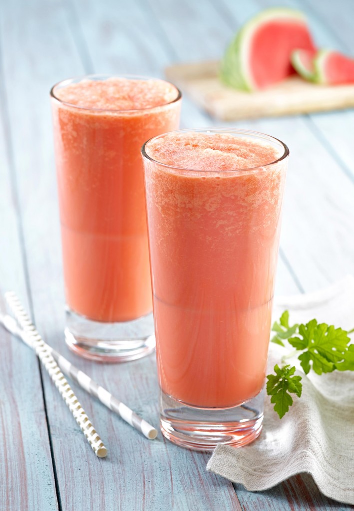 Collagen creamsicles (x2) in tall clear glasses with straws and greens garnish on side. Watermelon wedge and slices in background on wooden cutting board.