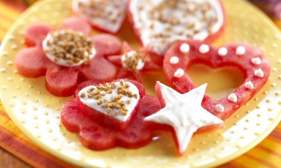 Frosted Watermelon Cutouts set on yellow plate with cutout cutters in background, also flowers in background