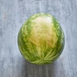 Whole watermelon shown on gray painted wooden table, depicting ground spot