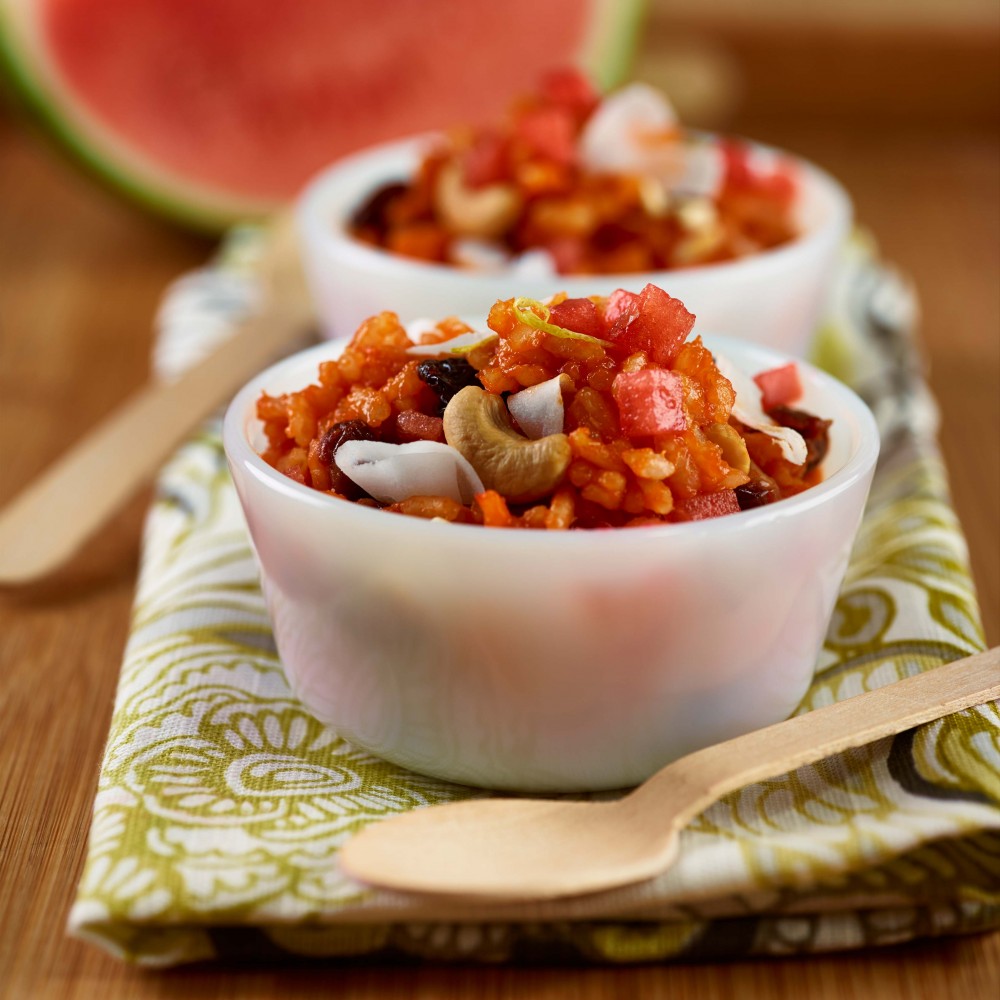 Thai watermelon coconut risotto set in two small white ramekins on green and white napkin with two wooden forks. Wedge of watermelon in background