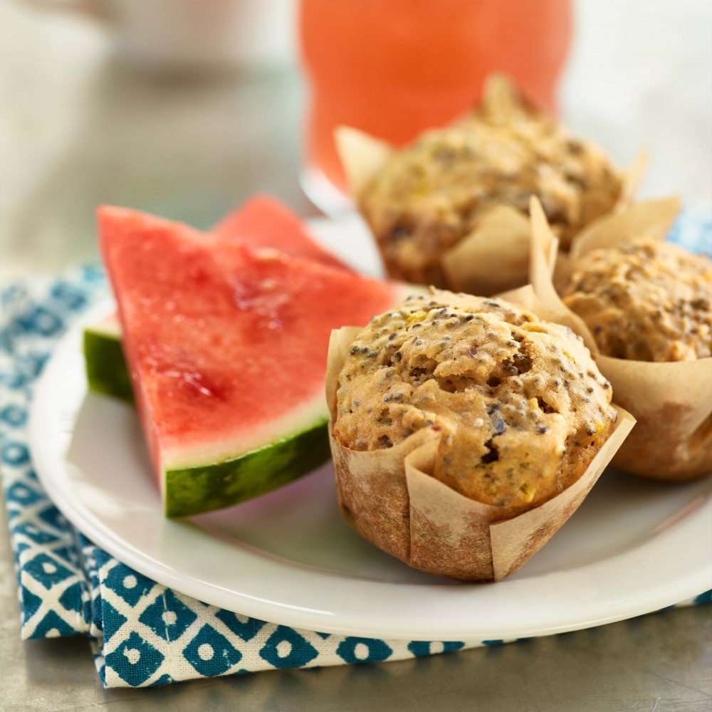 Watermelon Chia Seed Muffins (x3) set on small serving plate with two triangular watermelon slices. Cup of coffee and glass of watermelon juice in background