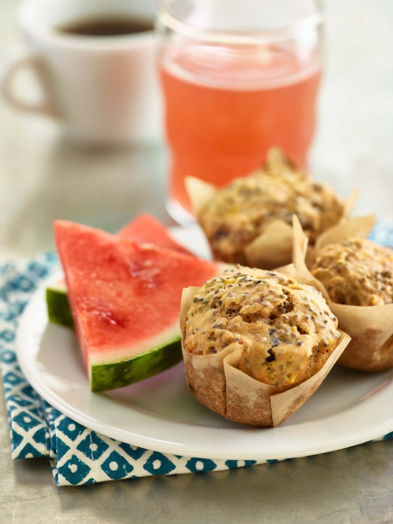 Watermelon Chia Seed Muffins (x3) set on small serving plate with two triangular watermelon slices. Cup of coffee and glass of watermelon juice in background