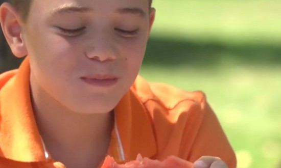 young boy in orange shirt eating and holding watermelon slice