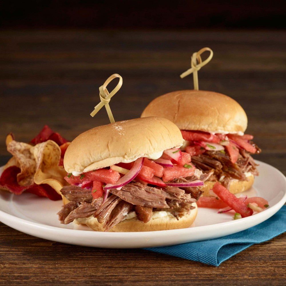 Lamb sliders (x2) set on plate with bamboo sticks to hold together. Chips served along side. Set on blue cloth napkin on wooden table