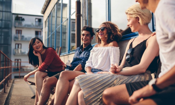 multiracial-group sitting at balcony of building smiling and laughing