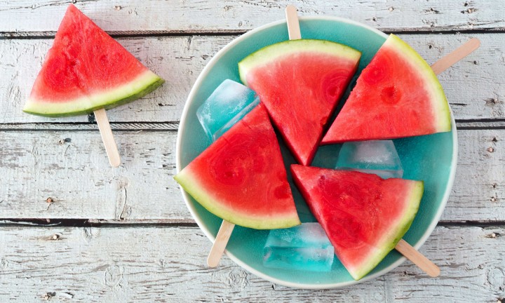 teal colored plate with 4 watermelon popsicles with ice on plate. One popsicle on side set on white painted table