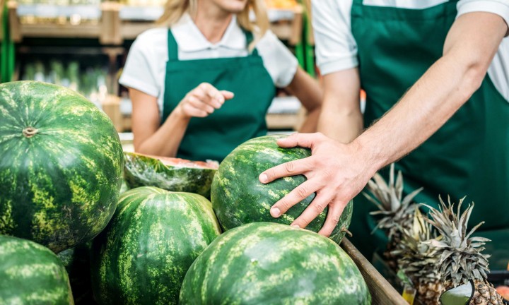 produce department employees, one man, one woman with woman pointing at watermelon, selection process