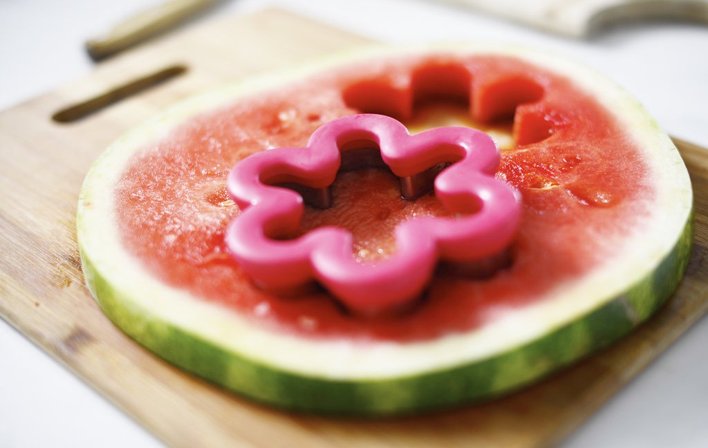 Round watermelon slice with cookie cutter in flower shape, set on wooden cutting board
