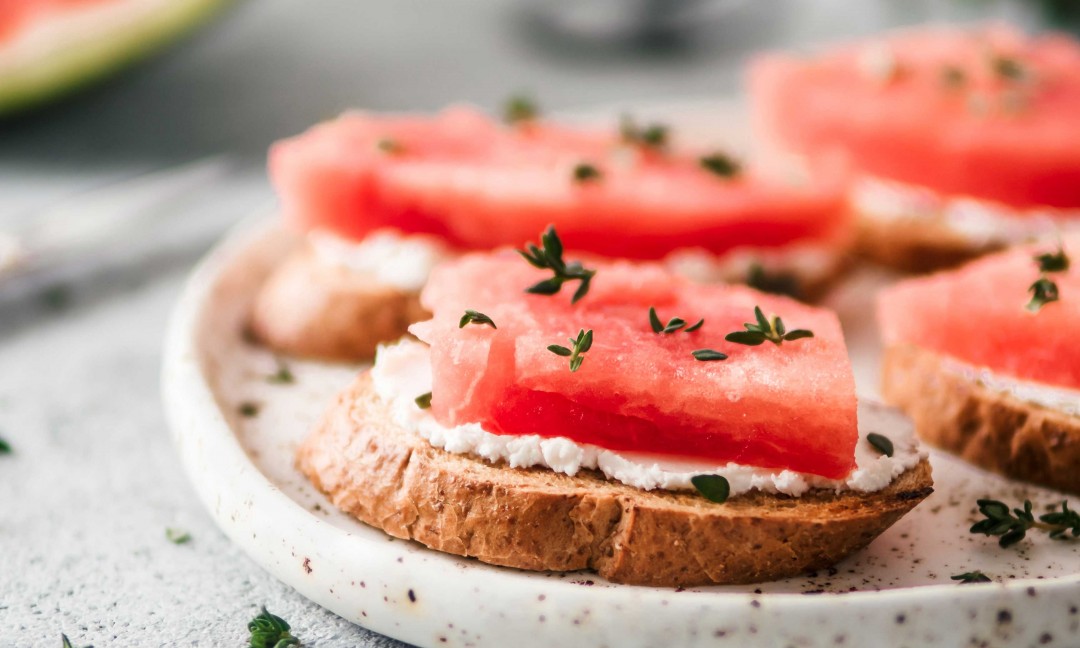 Toasts soft cheese watermelon fresh thyme set on plate with watermelon wedge in background