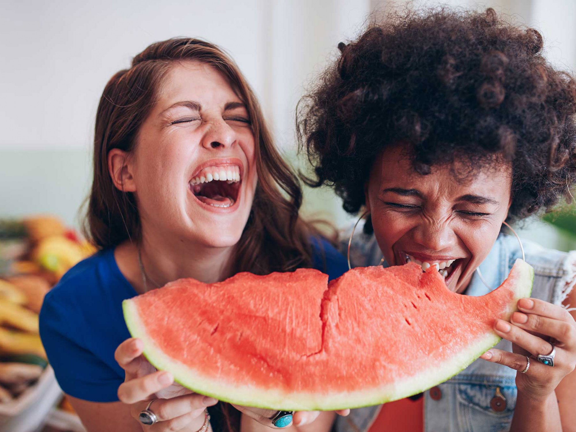 two women holding one oblong watermelon wedge, laughing