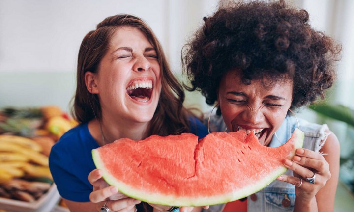 two women holding one oblong watermelon wedge, laughing