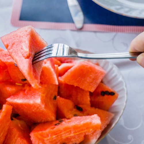 Watermelon on fork - plate of chunks (with seeds) with hand holding fork
