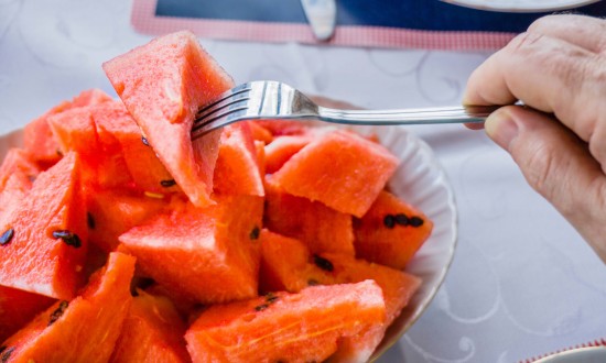 Watermelon on fork - plate of chunks (with seeds) with hand holding fork