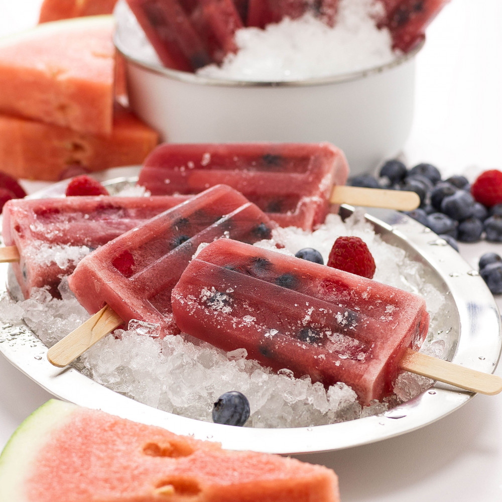 Berry Popsicles set in metal bowls with crushed ice. Garnished with blueberries, raspberries and triangular watermelon cuts on side.