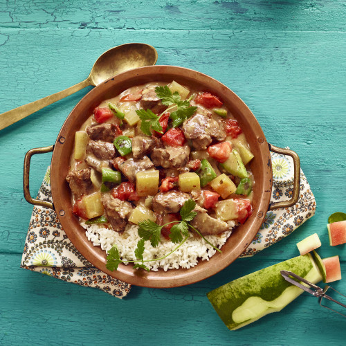 Watermelon Carne Guisada in bowl served over white rice. Cilantro garnish. Watermelon rind and peeler on side along with spoon.