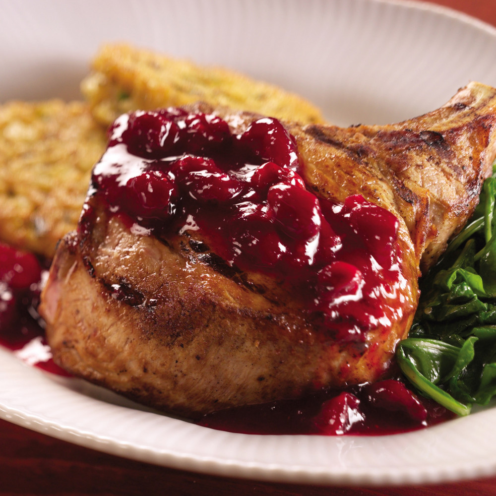 Cranberry glazed pork chops plated on round scalloped plate with steamed spinach and fried green tomatoes.
