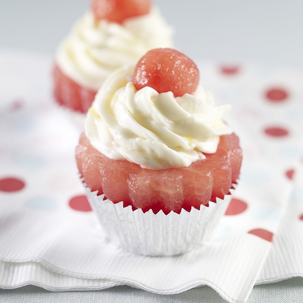 Two Watermelon Cupcakes in foil cupcake liners set on white with red polka-dot paper napkins. Each cupcake is topped with yogurt and small watermelon ball.