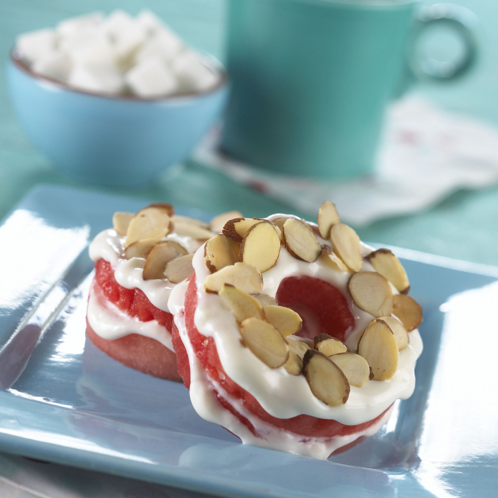 Watermelon donuts garnished with slivered almonds served on blue square plate with cup of coffee in background.