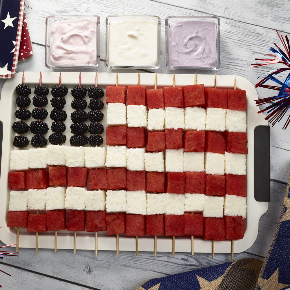 Flag kebobs, skewered to resemble American flag. Three clear condiment dishes containing flavored yogurts set with patriotic decorations and paper plates.