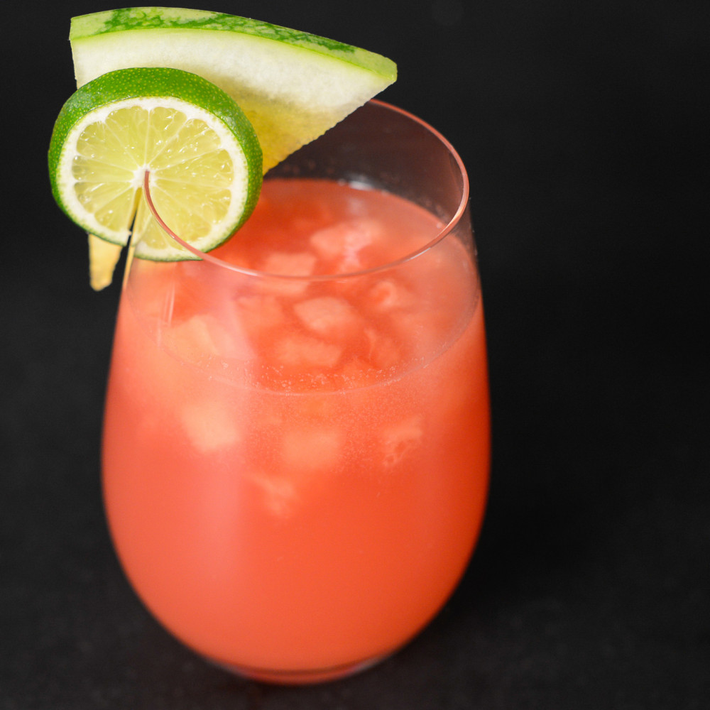 Watermelon Agua Fresca in clear glass with ice and garnished with lime and triangular cut of watermelon.