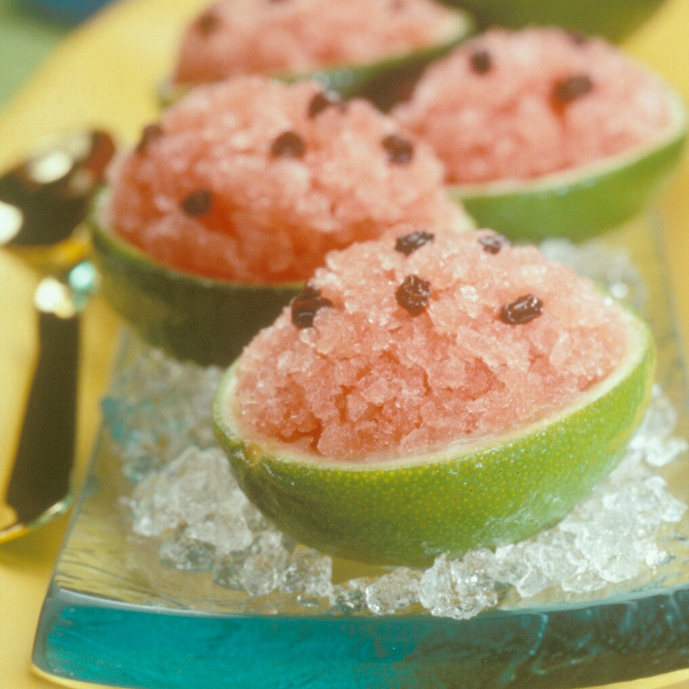 Five Granita Filled Cups garnished with raisins set on rectangular serving tray lined with crushed ice. Tray is set on yellow serving platter with spoon on side.