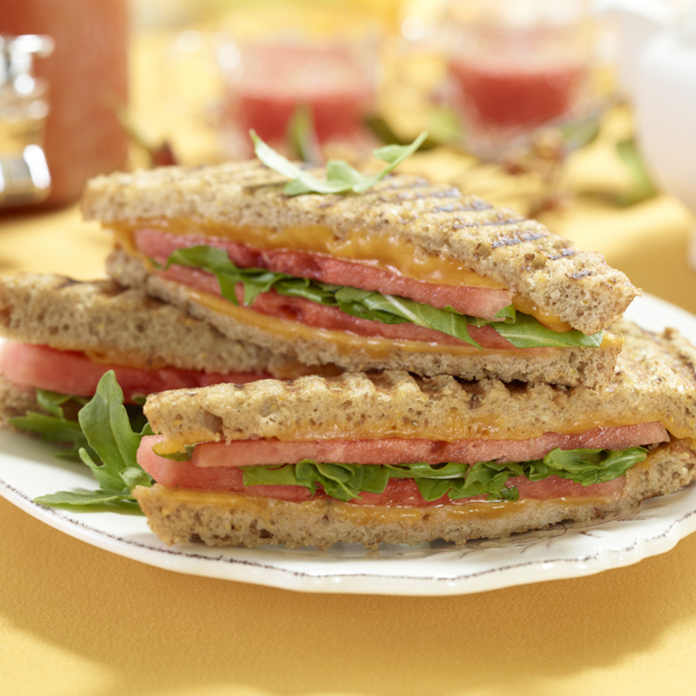 plated panini sandwich atop yellow tablecloth with dispenser-jar of aquafresca in background