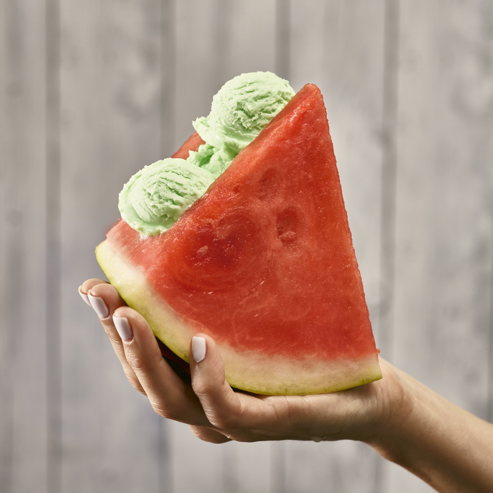 Watermelon Ice Cream Sandwich in hand. Two triangle cut of watermelon (with rind) with ice cream in center.