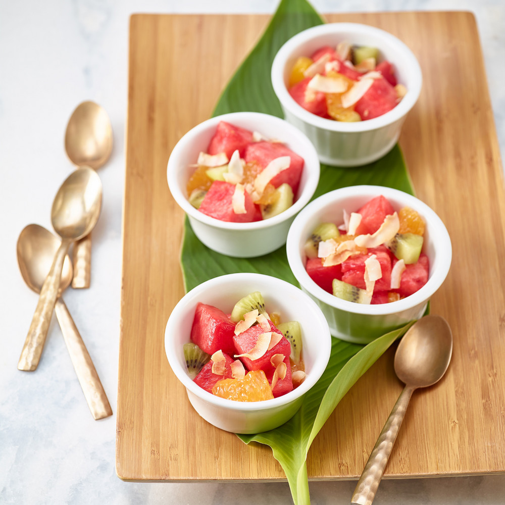 Island Fruit Salad served in three white ramekins on wooden cutting board with spoon on cutting board and 3 spoons on side.
